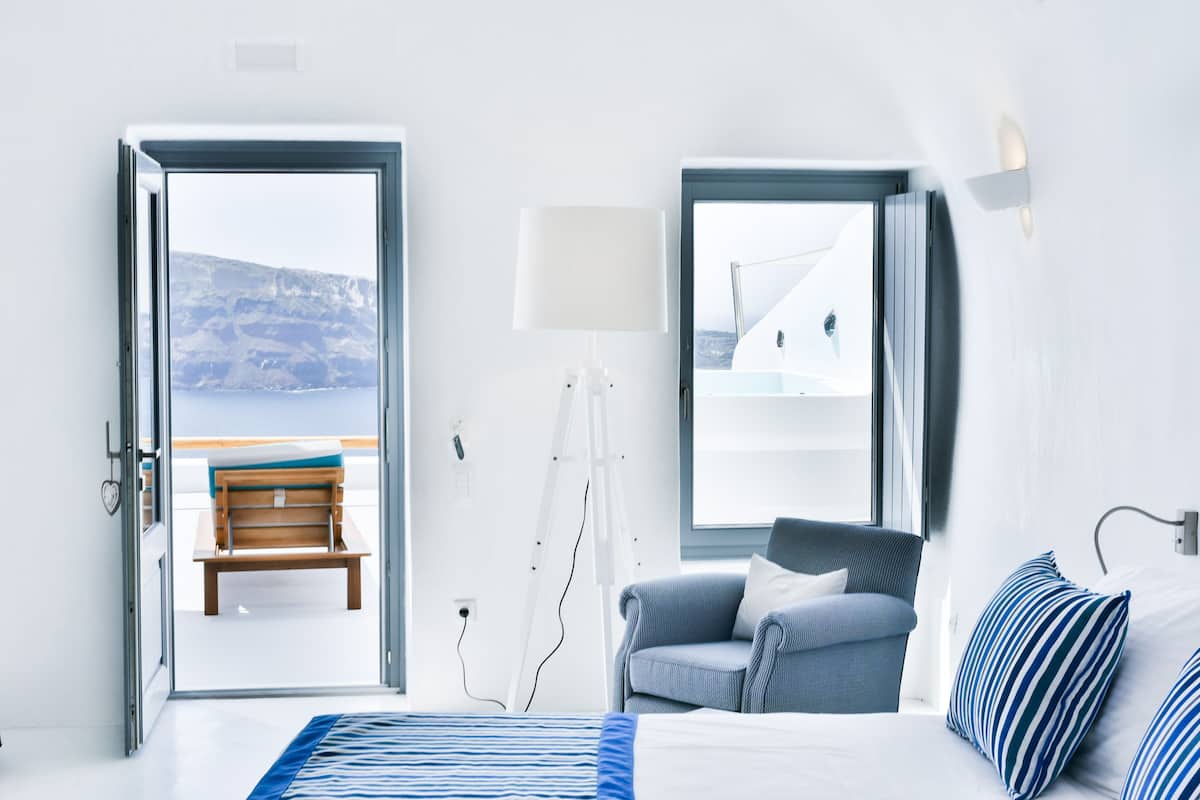 Una habitación de hotel con cama, una silla, un escritorio, una lámpara y vista al mar.
