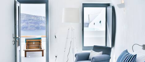 A hotel room with a bed, a chair, a desk, a lamp, and a view of the sea.