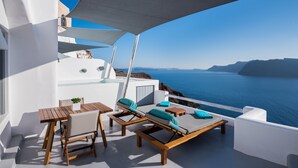 A balcony with wooden furniture, a small table, and a potted plant. - Maregio Suites (Santorini)
