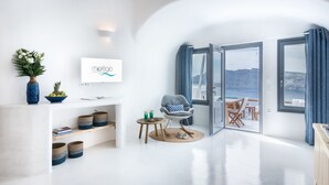 A modern living room with a white wall, a mounted TV, a blue vase, and a small table with drinks. - Maregio Suites (Santorini)