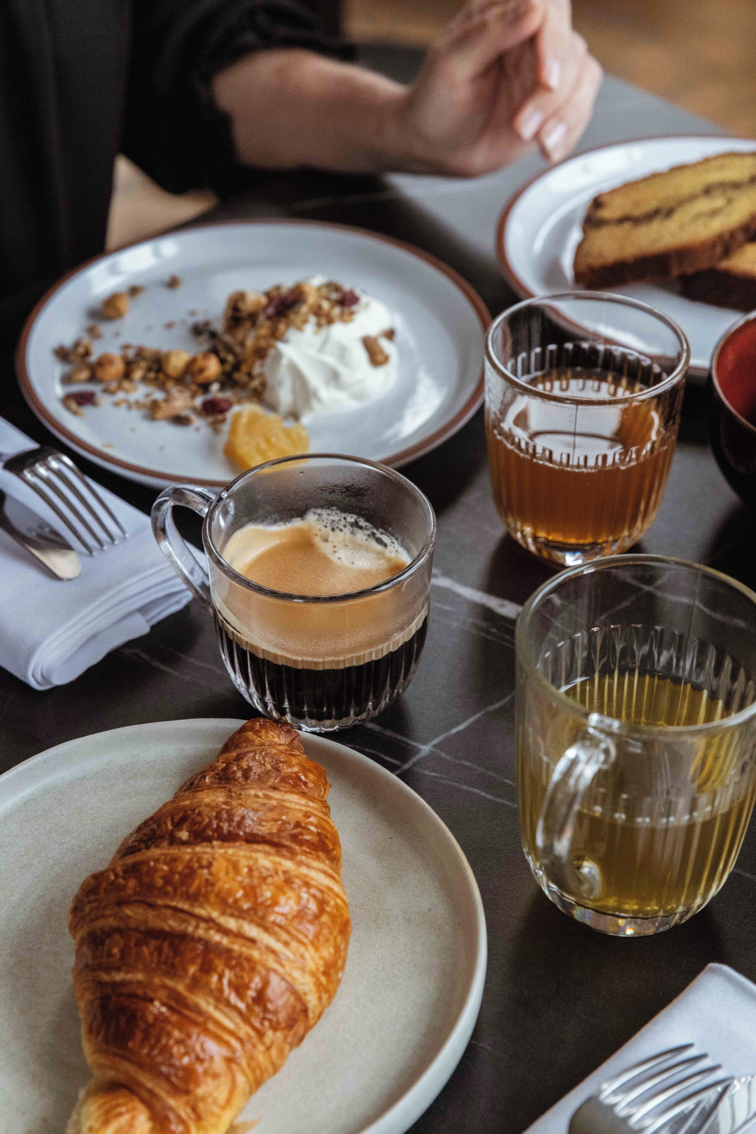 A dining table with plates of food, glasses of beverages, and a croissant.