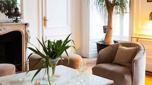 Una sala de estar con una mesa de centro de mármol, un sillón color beige, una planta grande en maceta y una chimenea.
