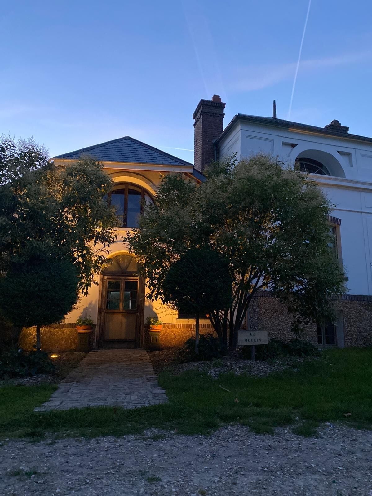 Una casa de dos plantas con fachada de piedra, una entrada central en arco y una chimenea.