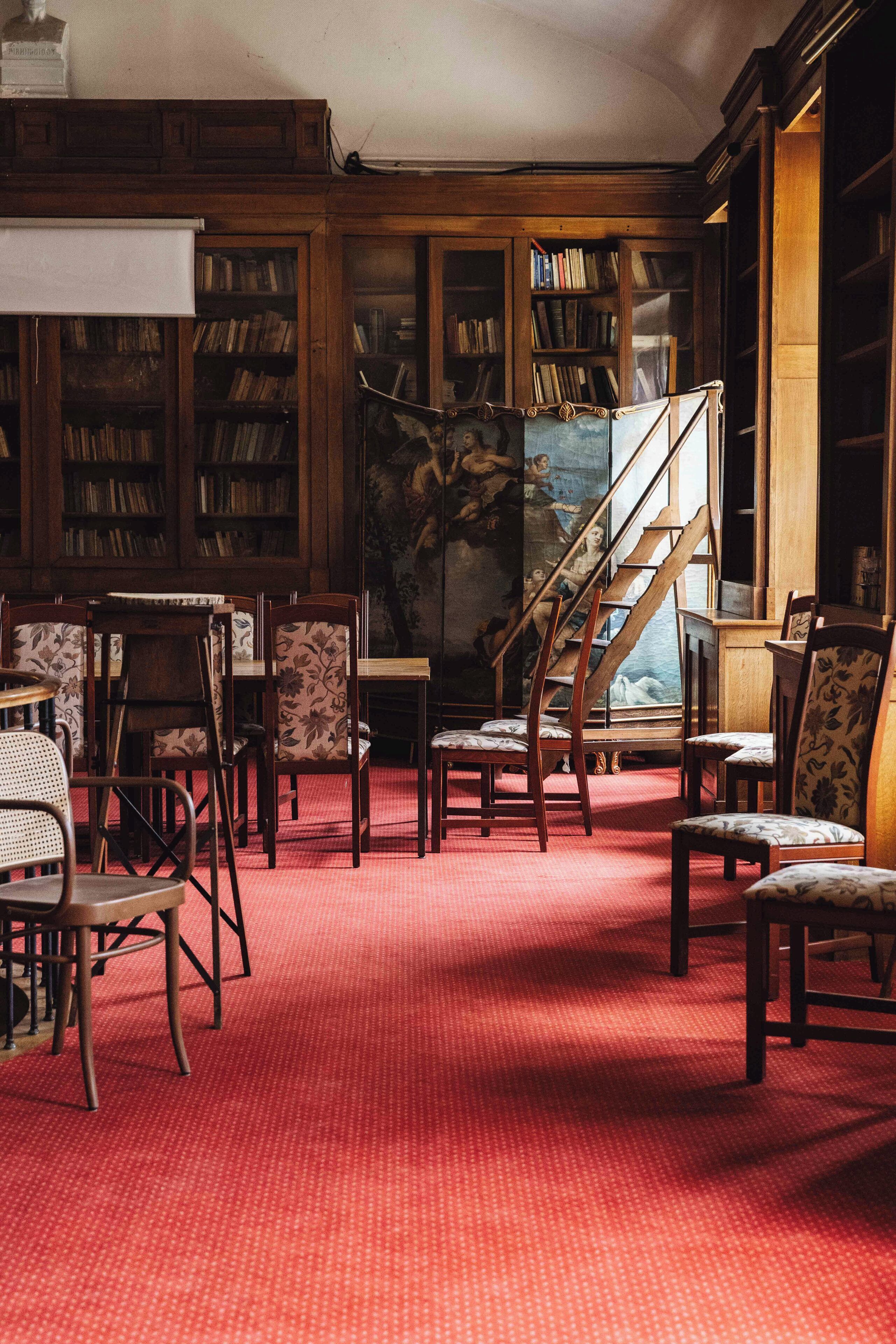 A library with wooden bookshelves, a red carpet, and a staircase.