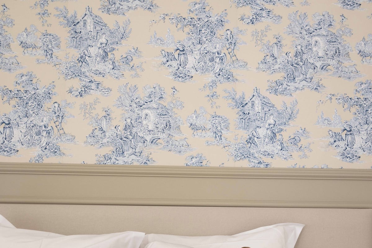 A bedroom with a bed, pillows, and a wall with a blue floral pattern.
