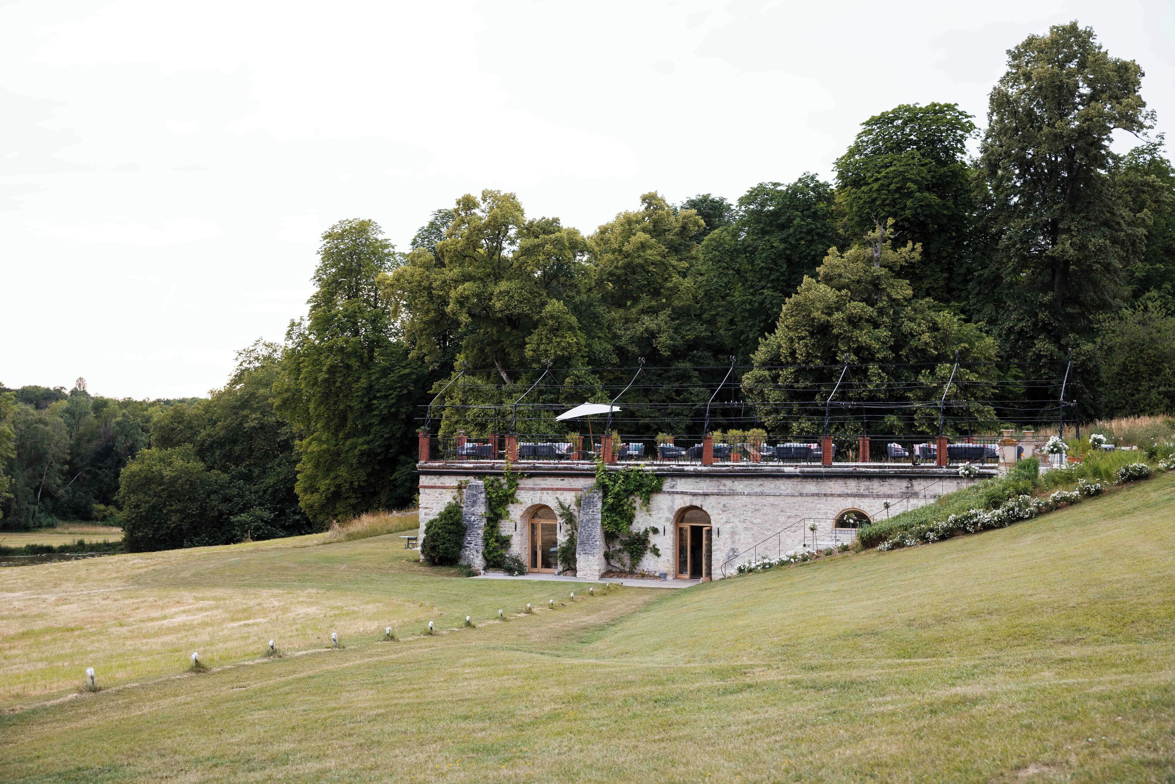A historic building with arched doorways, a covered walkway, and a lush green landscape.