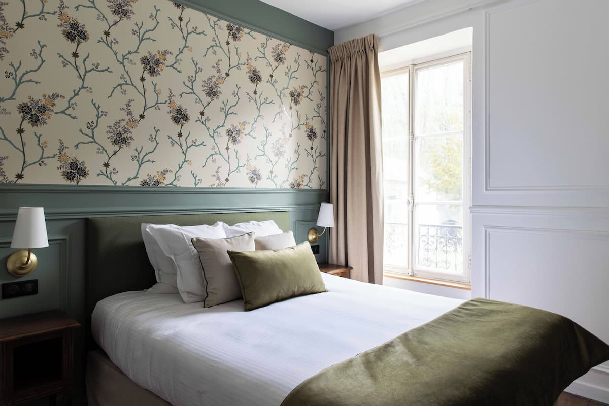 A neatly made bed with pillows, a nightstand with a lamp, and a window with curtains.
