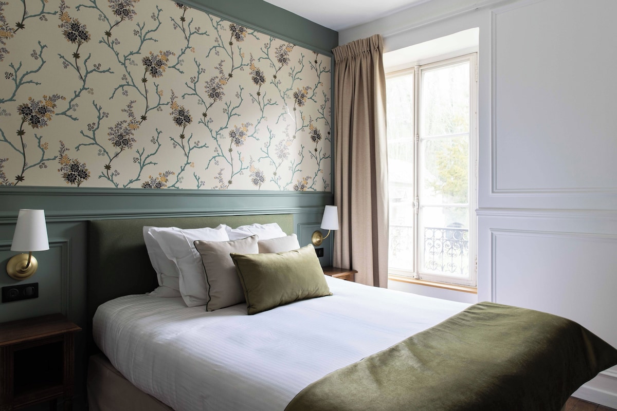 A neatly made bed with pillows, a nightstand with a lamp, and a window with curtains.