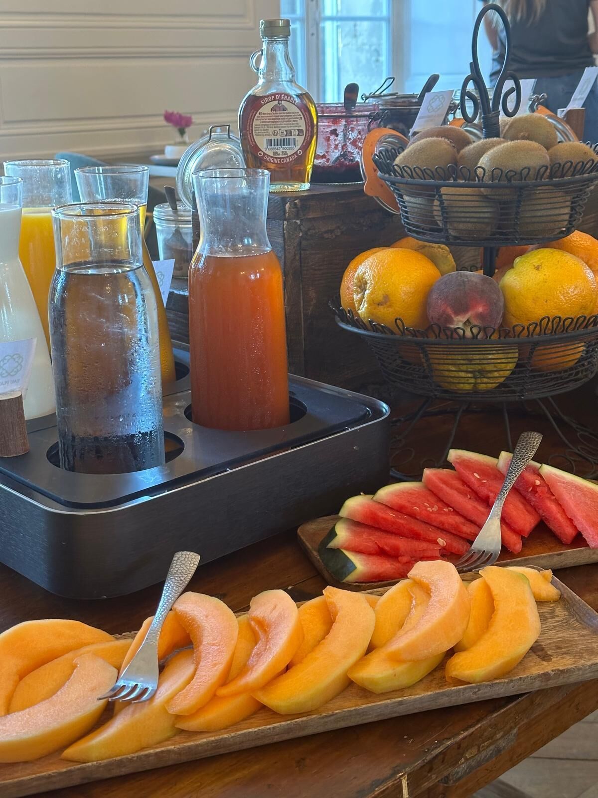 Un buffet de petit-déjeuner proposant divers fruits, des jus de fruits et un récipient de sirop.