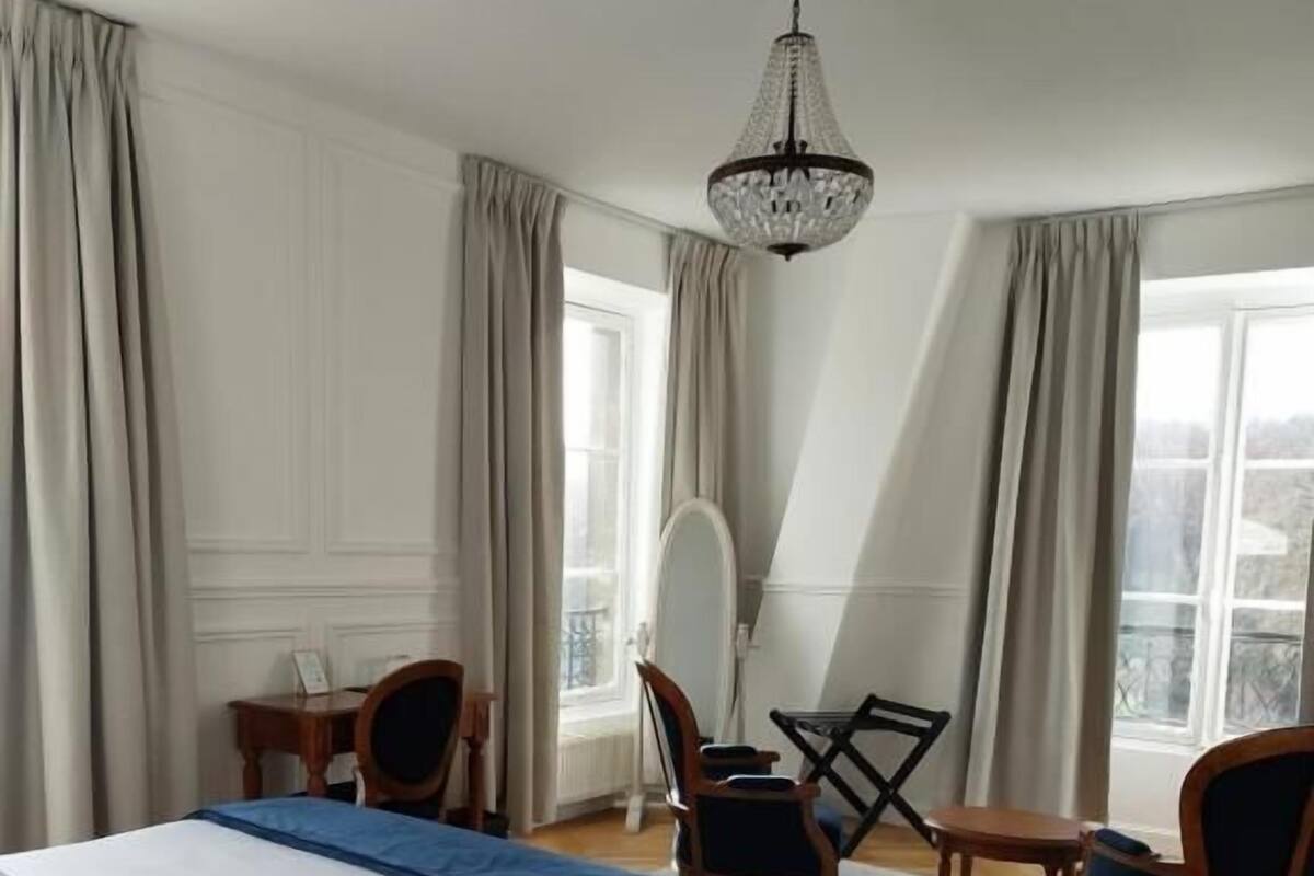 A hotel room with a large bed, a desk, a chair, and a chandelier.