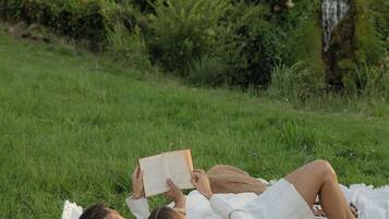 A person lying on a blanket in a grassy area with trees and a waterfall in the background.