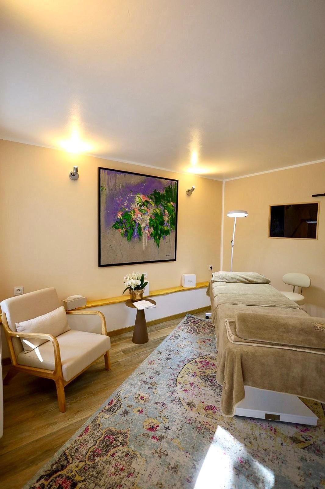 Habitació d'hotel moderna amb un sofà beix, una taula rodona petita amb un ram de flors, un quadre abstracte gran a la paret i un llit amb un mantell beix.