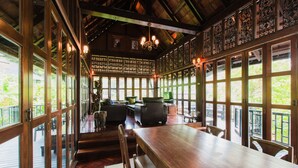 Ett rymligt matområde med ett långt träbord och stolar, stora fönster med dekorativa galler och en kristallkrona.