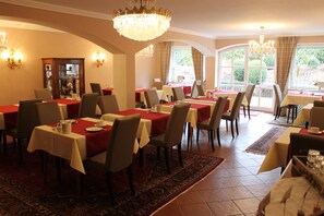 A dining area with multiple tables, chairs, and a chandelier. - Hotel garni Bellevue (Bad Fuessing)