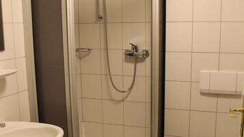 A shower enclosure with a handheld showerhead and a handheld faucet.