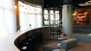 A modern bar area with a curved counter, multiple stools, and a seating area with sofas and round tables. - Tido Hostel Penang (George Town)