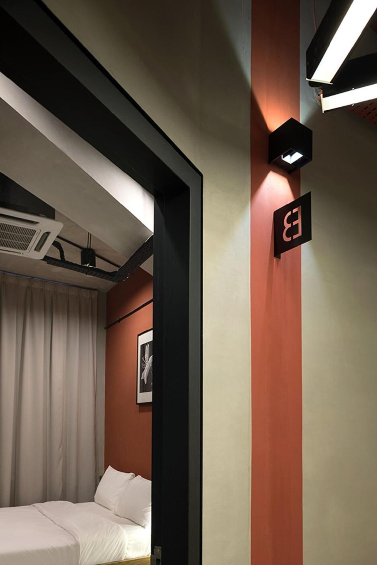 A hotel room with a bed, a wall-mounted air conditioner, and a sign with a letter 'B'.