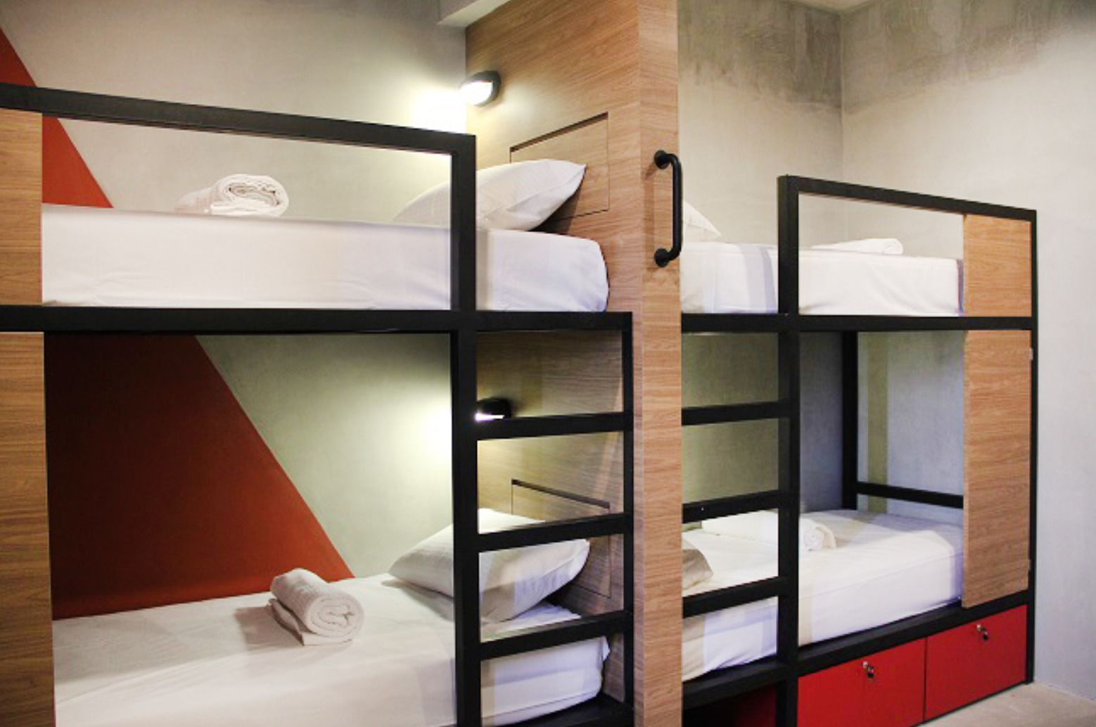 A bunk bed room with wooden headboards, a red cabinet, and a wall-mounted light.
