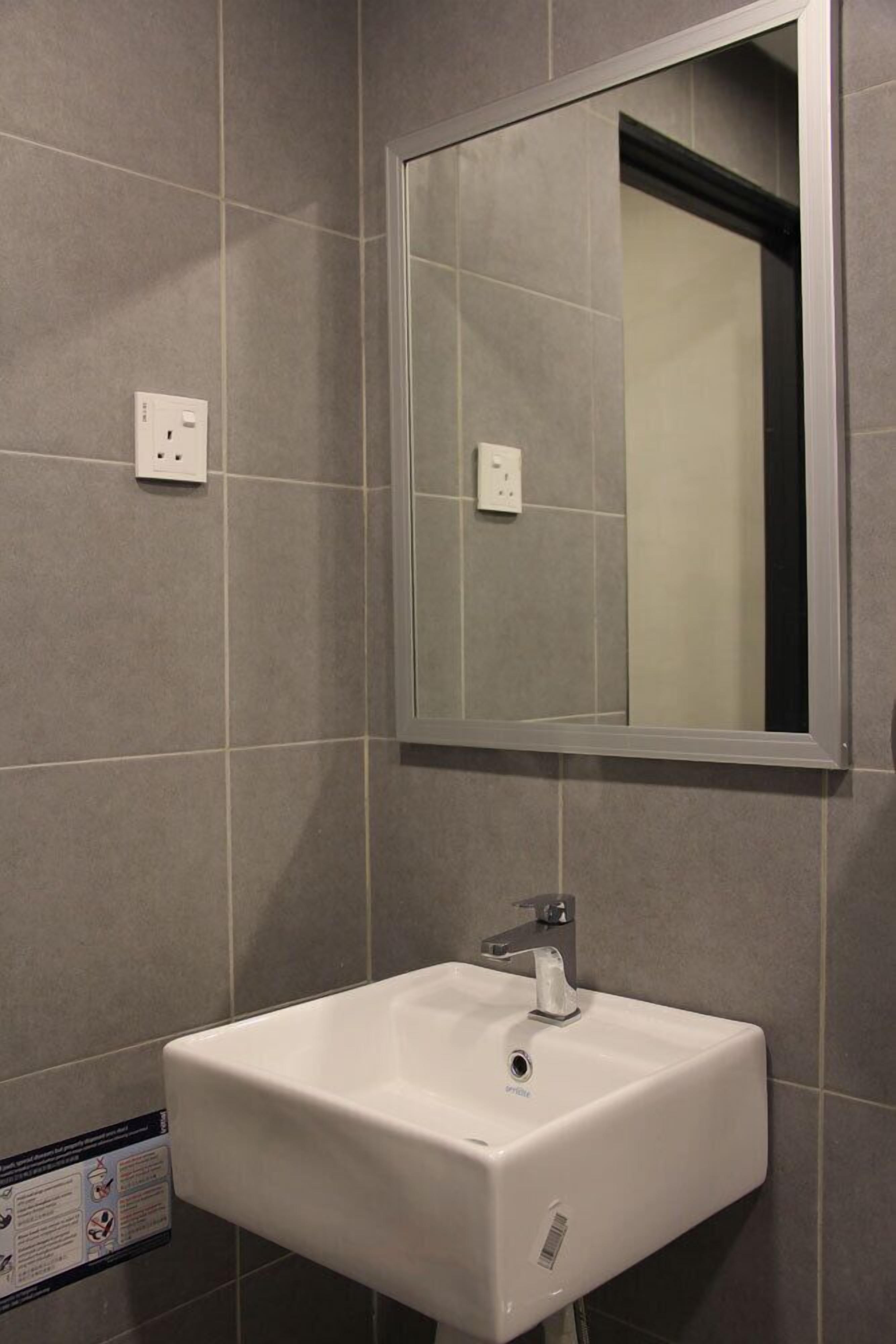 A bathroom with a white sink, a mirror, and two electrical outlets on the wall.