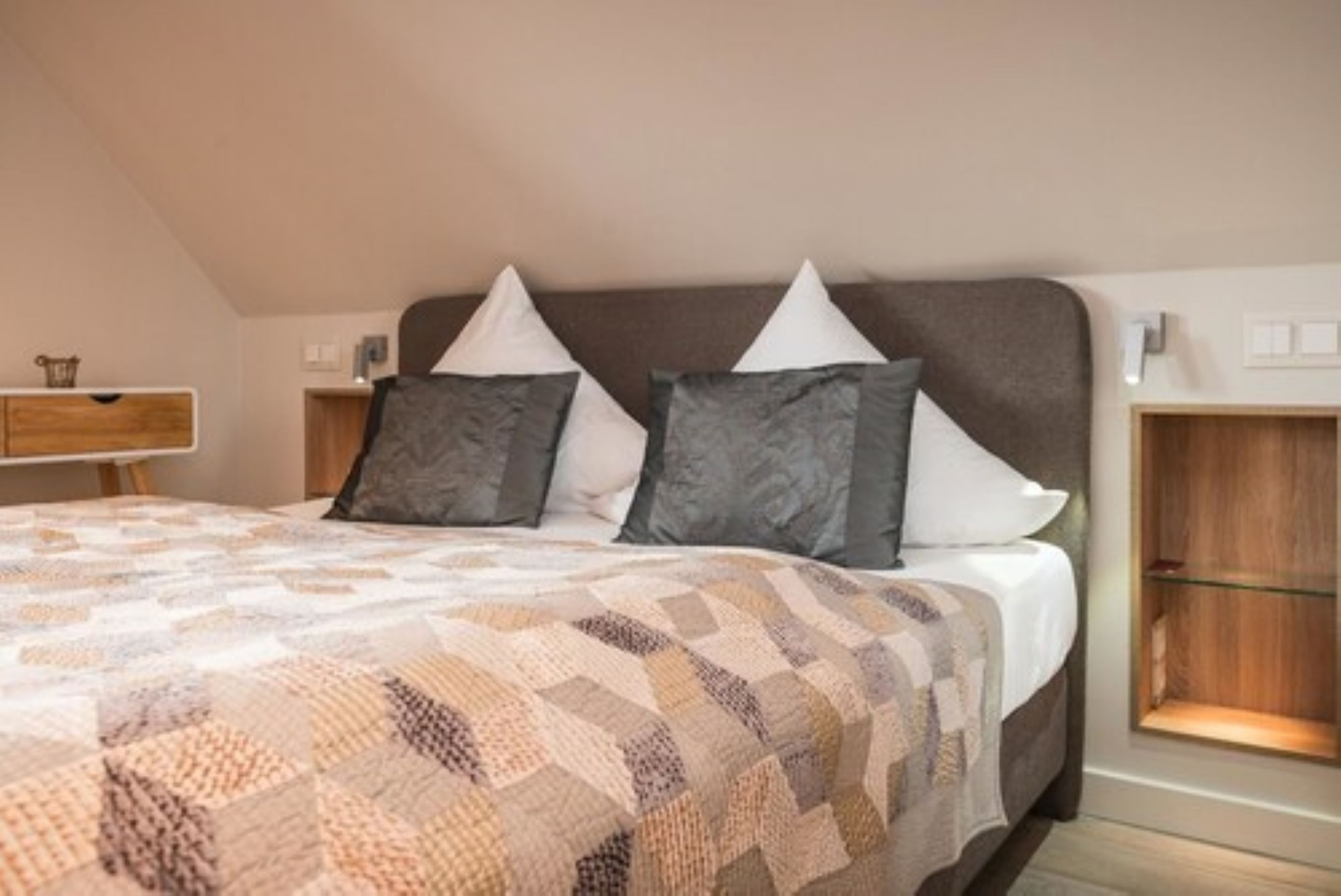 A bedroom with a large bed, two pillows, a wooden nightstand, and a bedside table with a lamp.