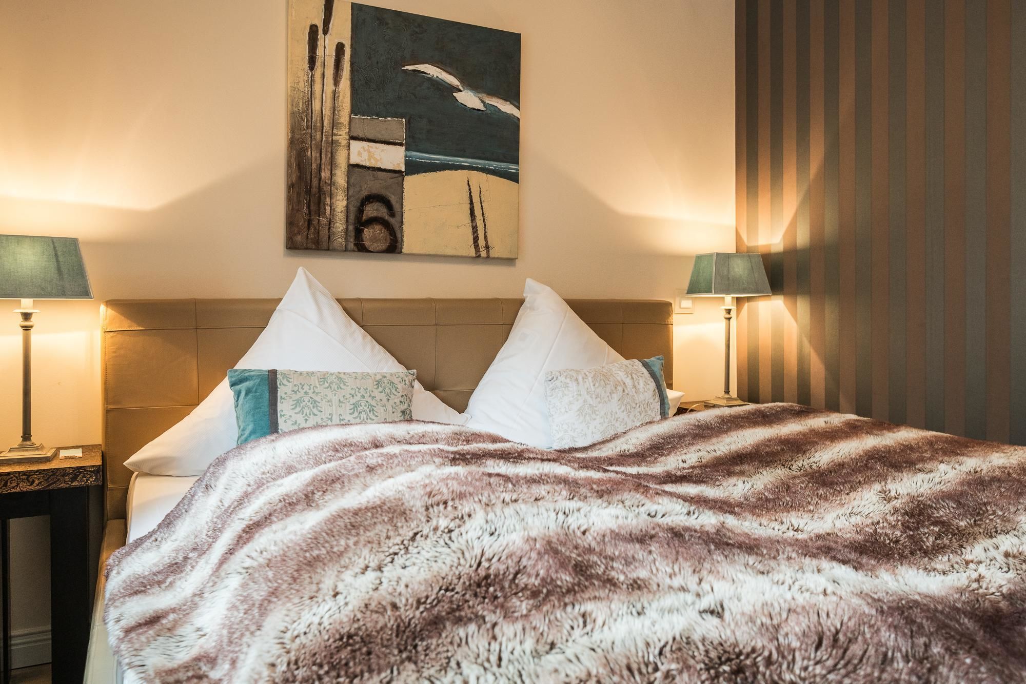 A hotel room with a bed, two nightstands, lamps, a painting, and a curtain.