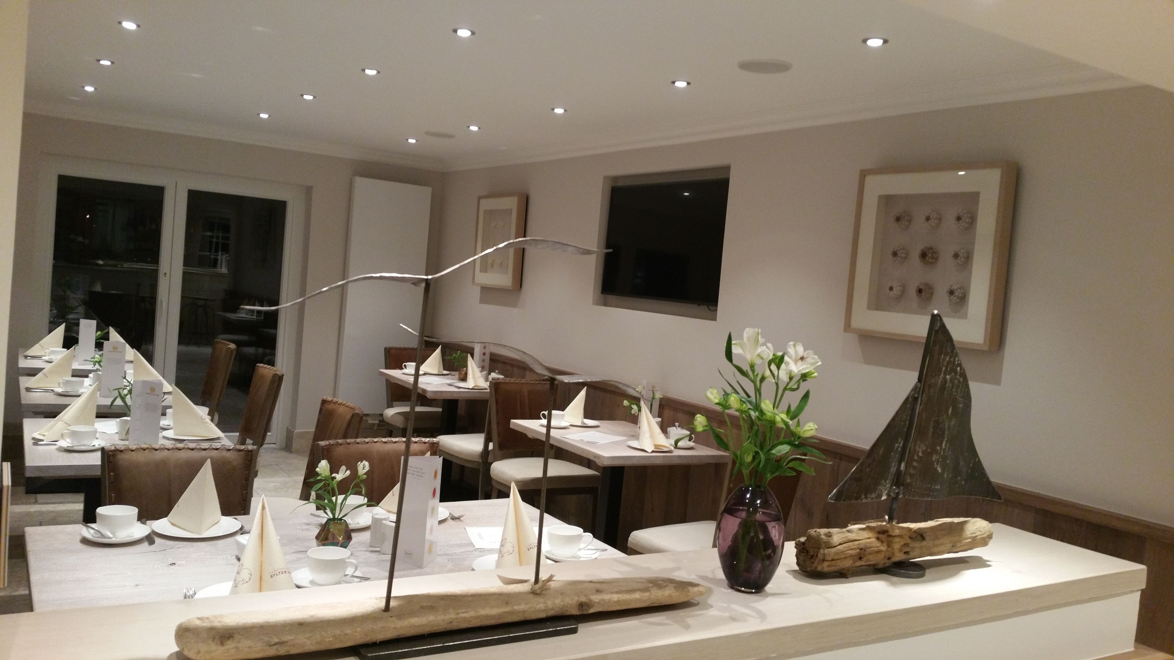Un espace de restauration moderne, avec des tables dressées pour le repas, agrémenté d’une pièce décorative centrale et d’un vase rempli de fleurs.