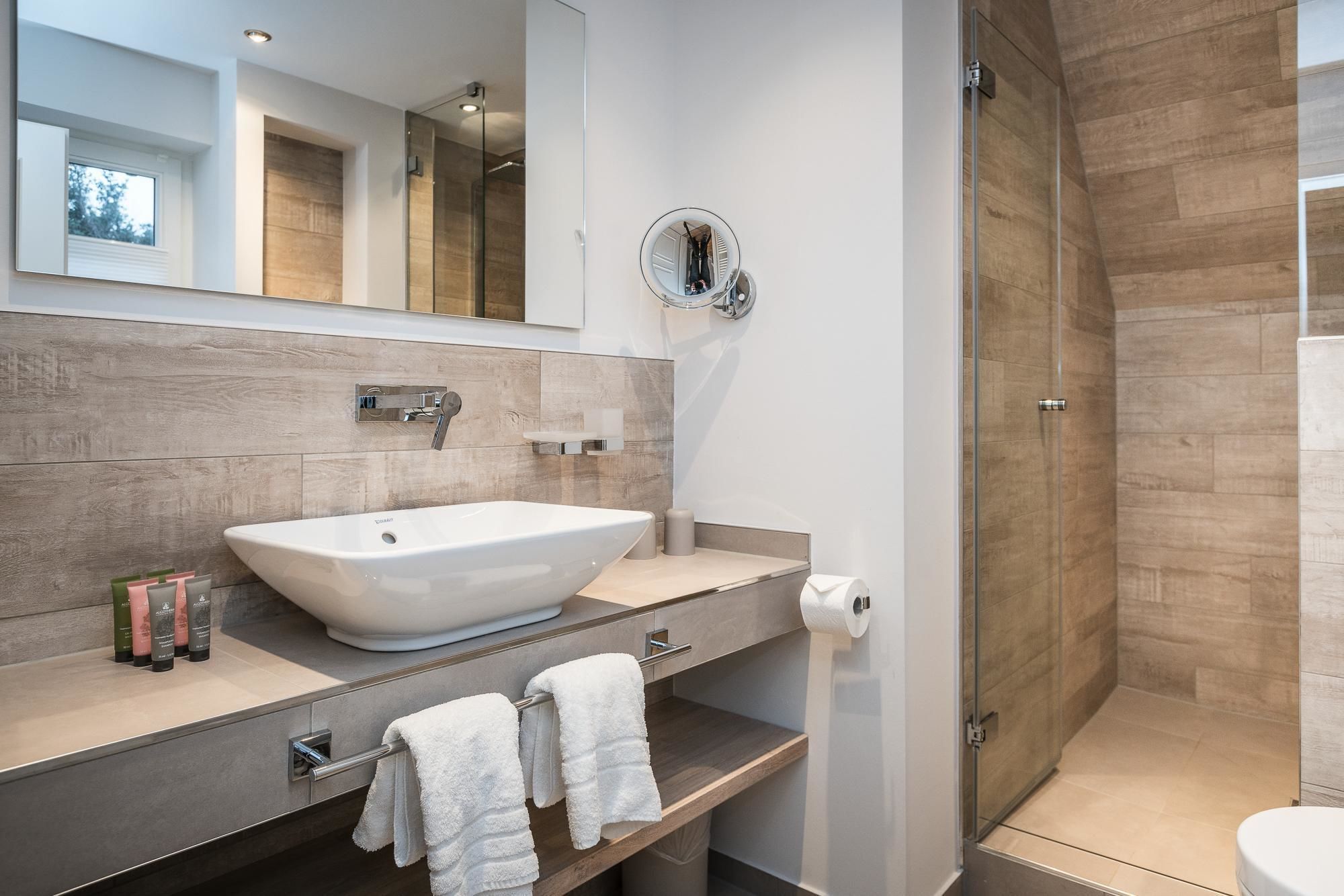 A modern bathroom with a large vessel sink, a mirror, and a walk-in shower.