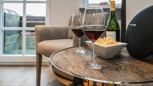 Ett runt träbord med två vinglas, en vinflaska och en skål med snacks i ett modernt rum med ett stort fönster.