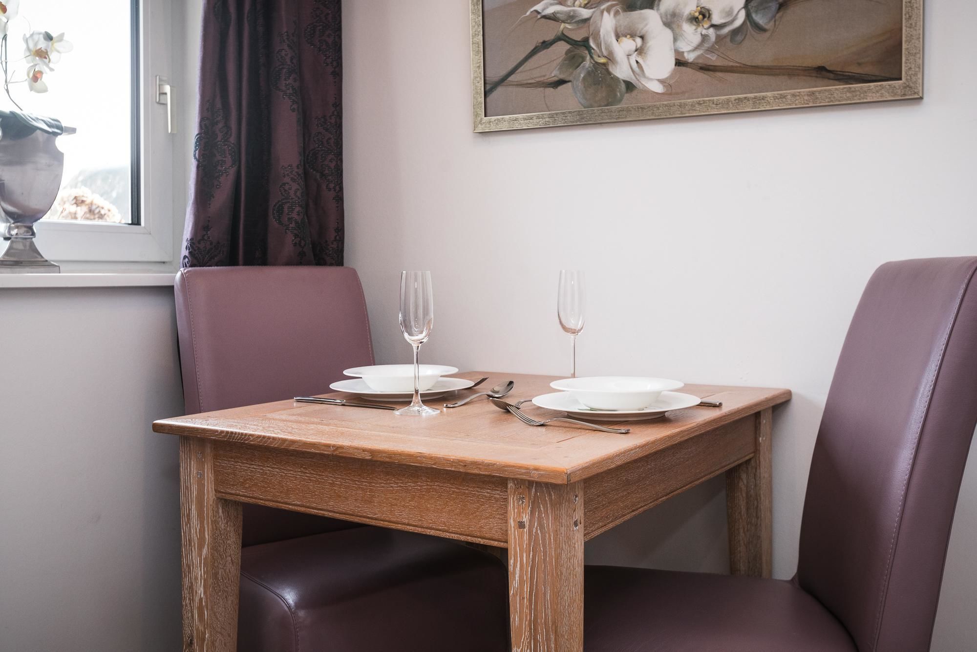 A dining table set for two with a painting above it.
