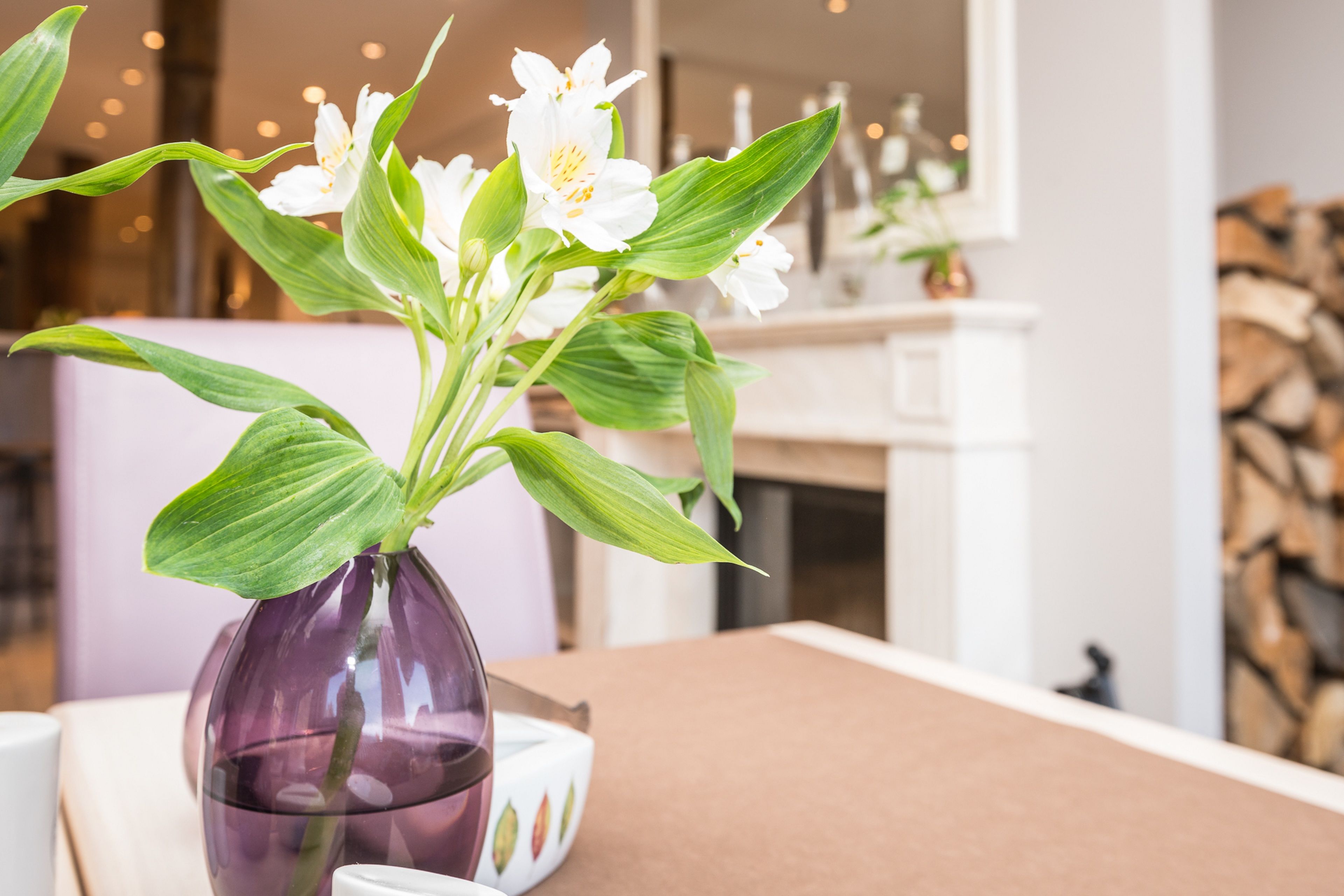 Une table à manger sur laquelle se trouve un vase violet contenant des fleurs blanches.
