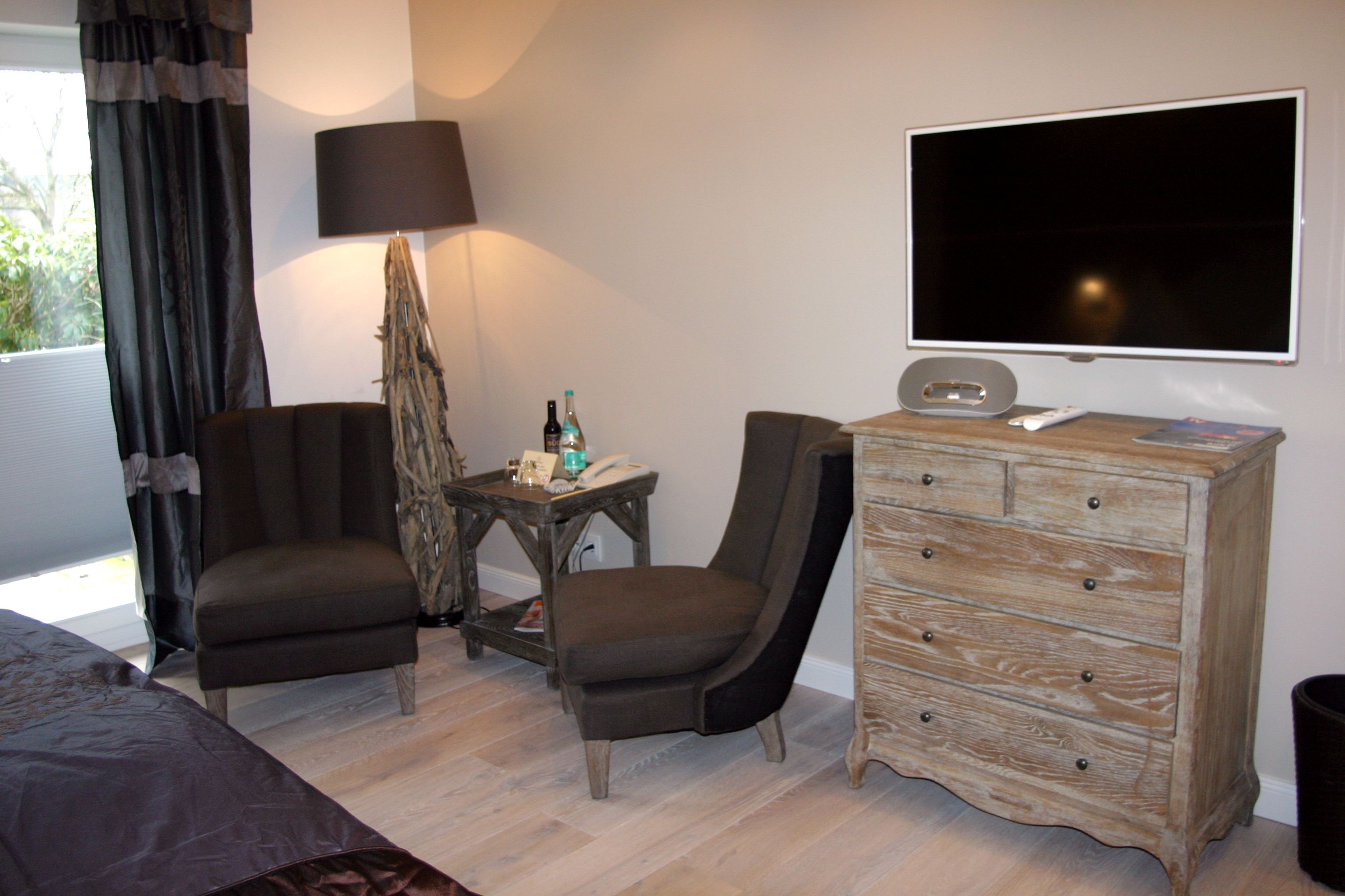 A hotel room with a bed, two armchairs, a wooden dresser, a television, and a lamp.