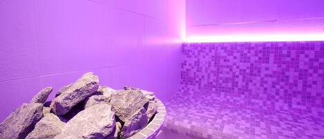 A bathroom with a purple hue, a tiled wall, and a stone basin.