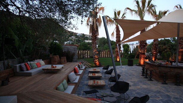 Un patio al aire libre con mobiliario de madera, suelo de piedra y una zona de estar con cojines.