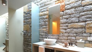 Un baño con pared de piedra, un lavamanos blanco, un espejo y un perchero para toallas.