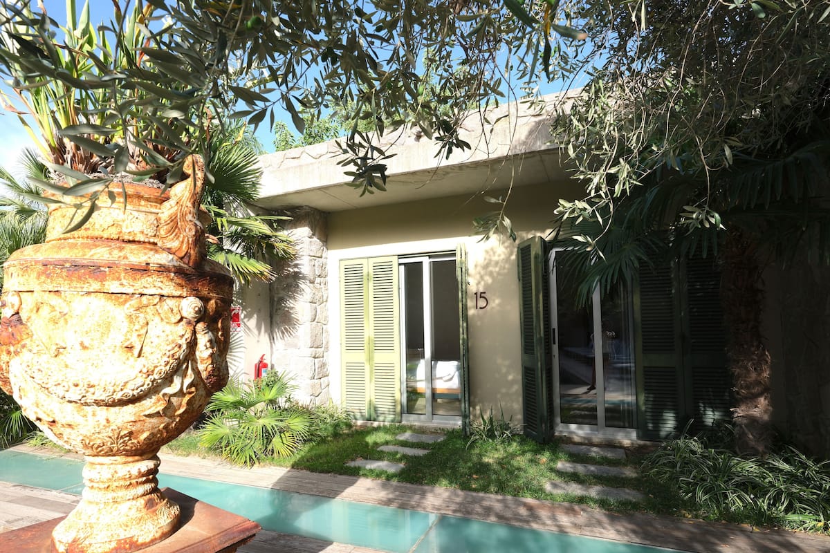 Una casa con piscina, contraventanas verdes y una gran urna decorativa al frente.