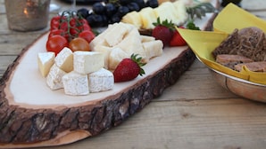 Una mesa de madera con una bandeja de quesos, uvas, fresas y una botella de aceite de oliva.