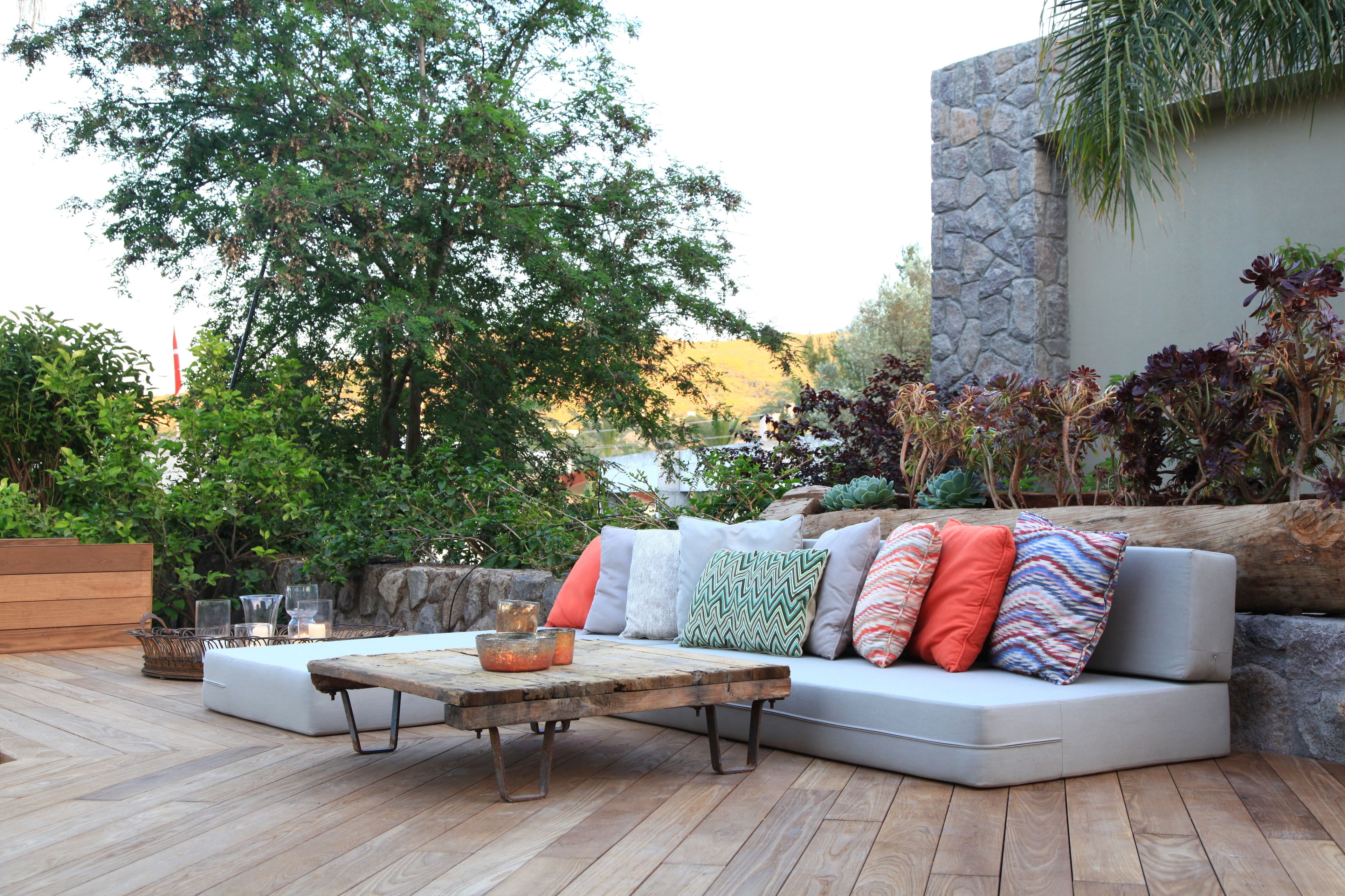 An outdoor seating area with a wooden table, cushioned sofa, and various decorative pillows.