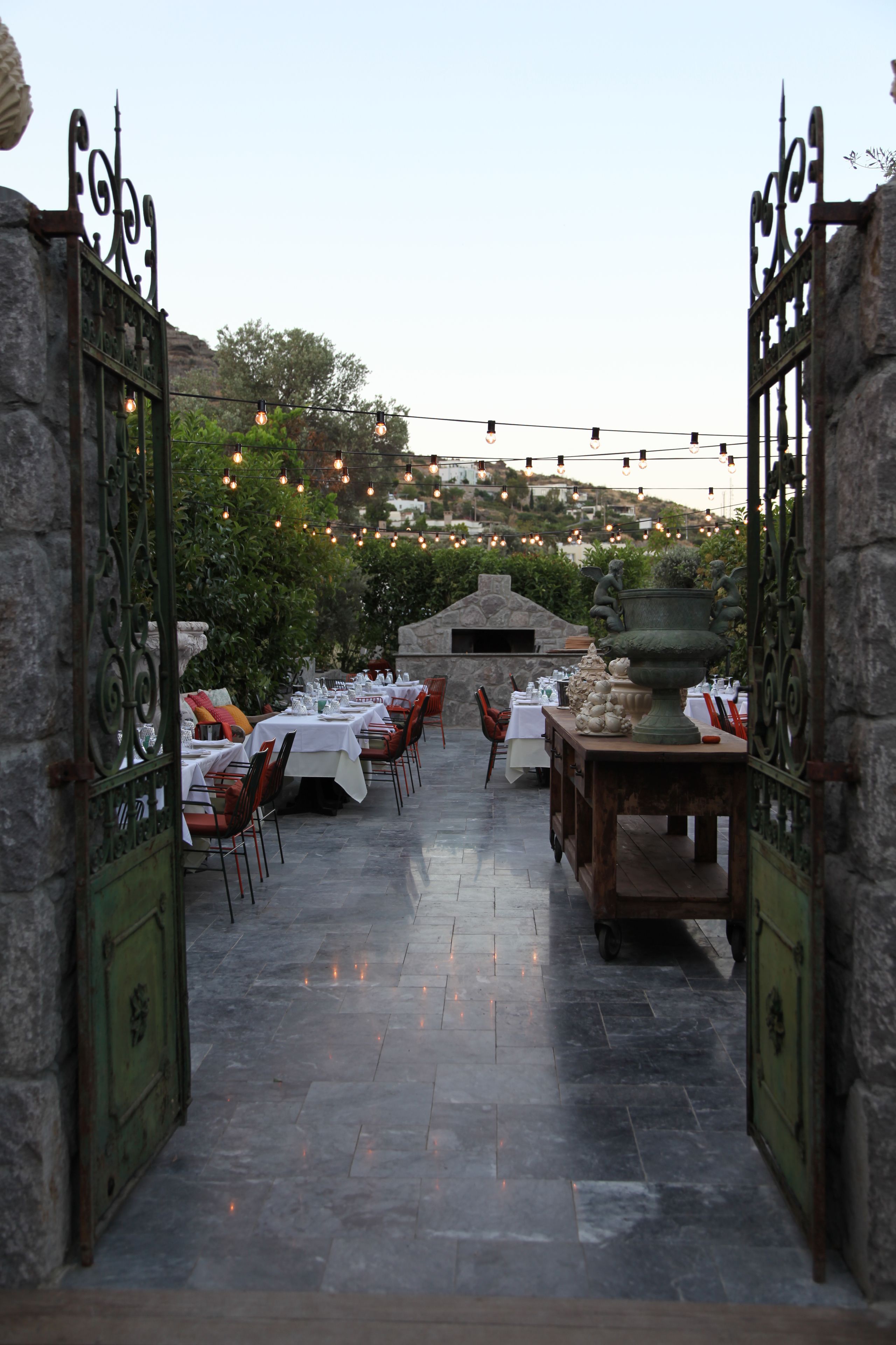 An outdoor dining area with stone walls, tables set for dining, and string lights overhead.