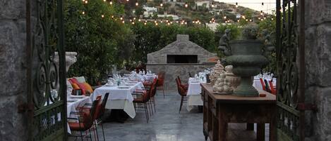An outdoor dining area with stone walls, tables set for dining, and string lights overhead.