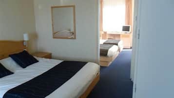 Habitación de hotel con una cama individual, una mesita de noche, un espejo y vistas a otra habitación con un escritorio y una silla.