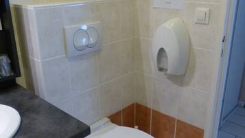 Un baño con inodoro, secamanos y dispensador de papel en la pared.