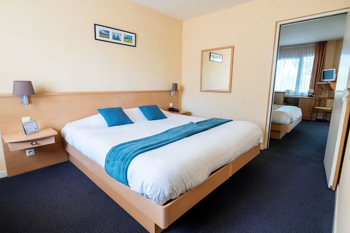 Ein Hotelzimmer mit einem großen Bett, zwei Nachttischen, einem Schreibtisch und einem Spiegel.