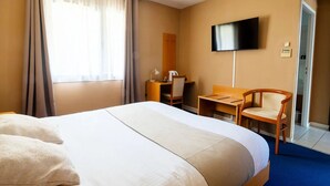 Habitación de hotel con una cama grande, un escritorio con silla, televisión en la pared y una puerta que da a otra habitación.