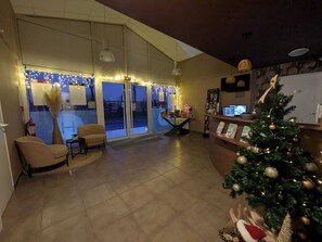A spacious lobby with a large window, a Christmas tree, and a reception desk. - Hotel L'Océane Angers Parc Expo (Rives-du-Loir-en-Anjou)