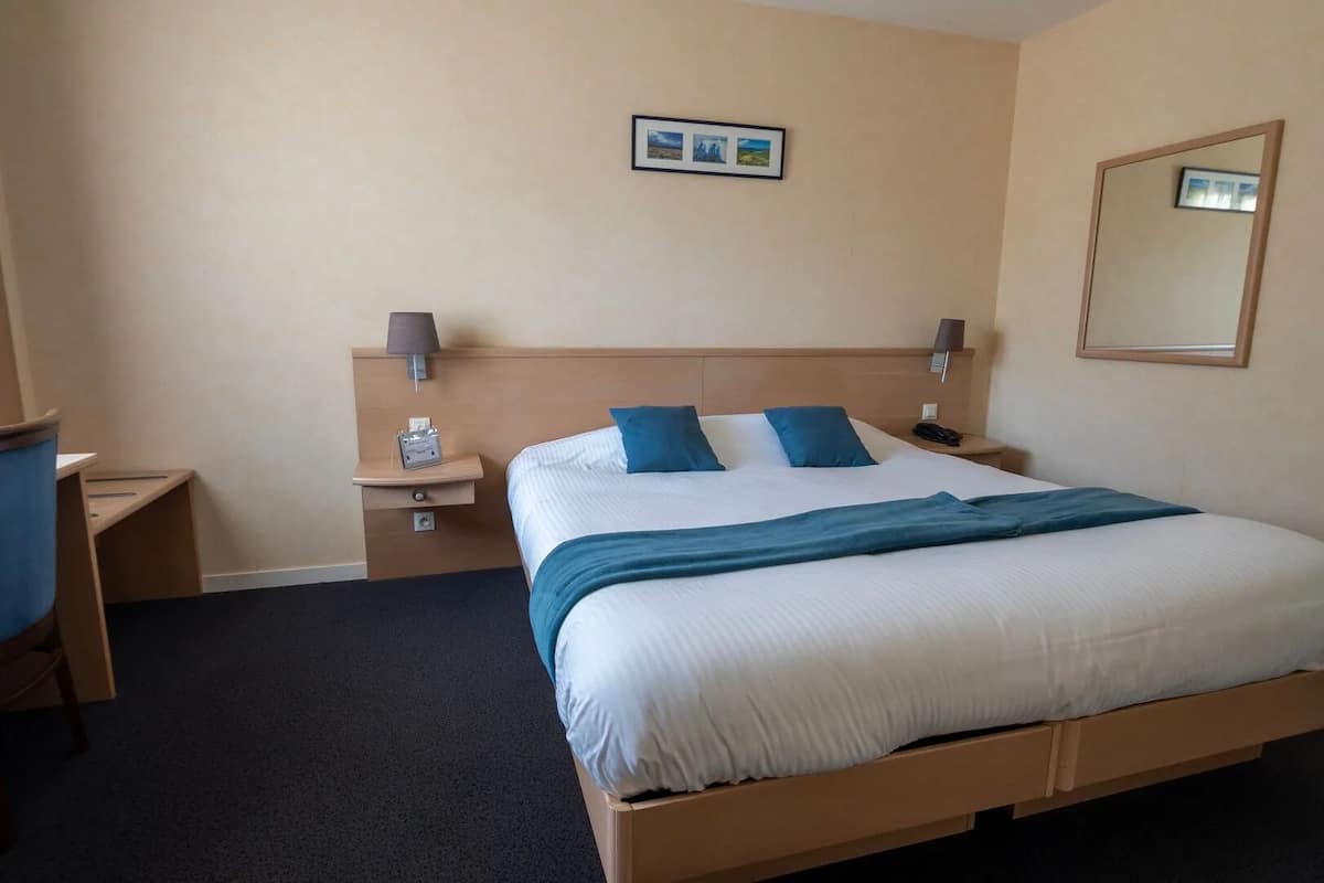 Ein Hotelzimmer mit Bett, Schreibtisch, Stuhl, Nachttisch und Spiegel.