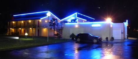 A building with a car parked in front, illuminated by blue lights.