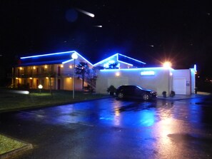 A building with a car parked in front, illuminated by blue lights. - Hotel L'Océane Angers Parc Expo (Rives-du-Loir-en-Anjou)