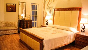 A bedroom with a wooden bed, a nightstand with a lamp, a dresser, a sofa, and a door. - Lahore Guest House (Lahore)