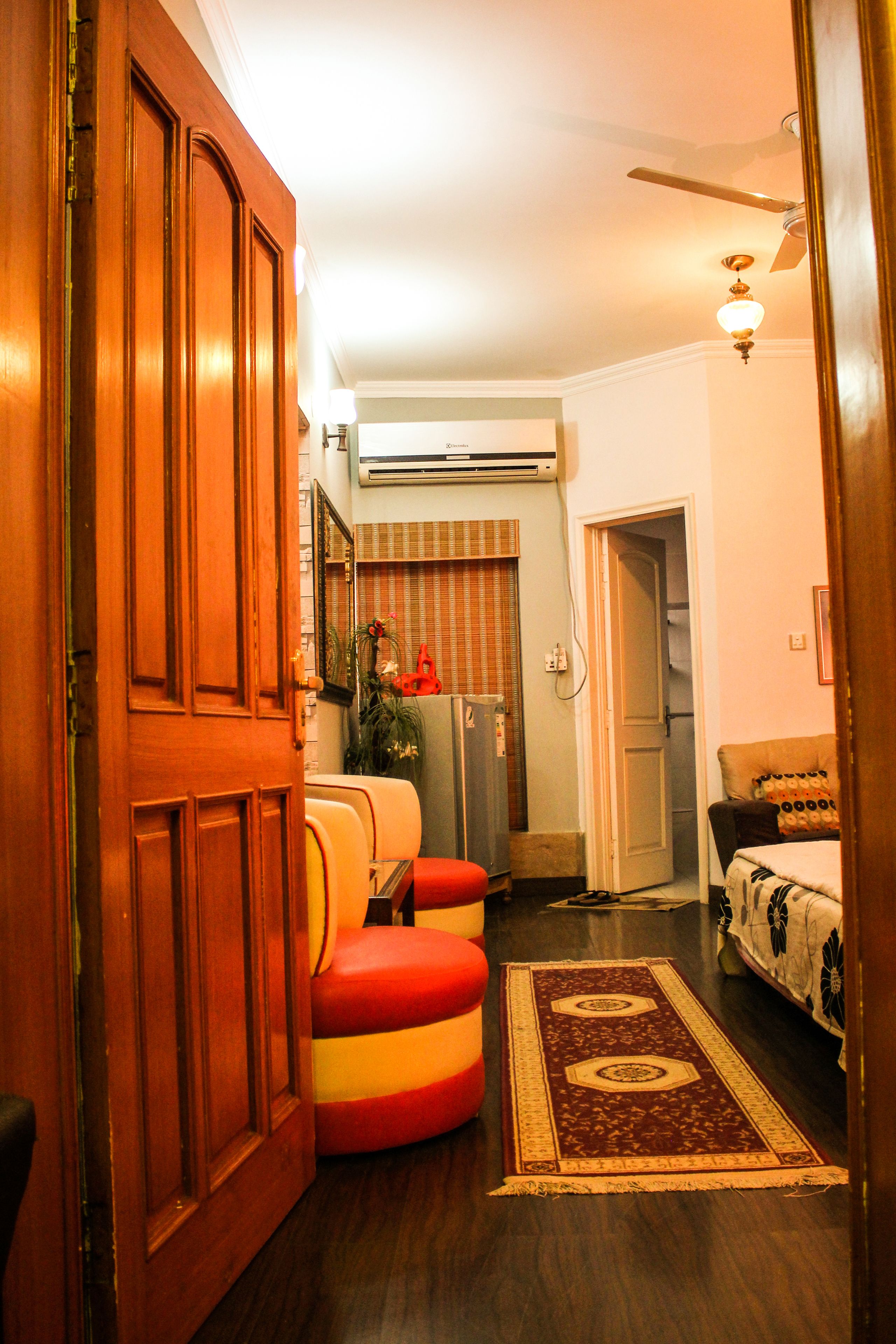A room with a wooden door, a ceiling fan, a radiator, a sofa, a patterned rug, and a bed with a patterned bedspread.