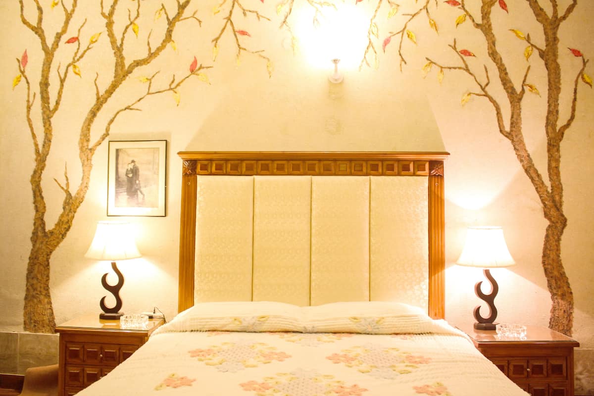 Un dormitorio con una cama, dos mesitas de noche, una lámpara de pared y un cuadro enmarcado.